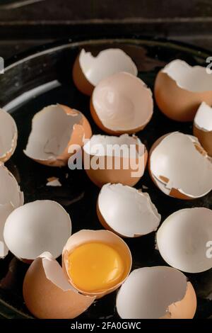 broken eggs on a platter, empty egg shells, one yellow egg yolk still in the half shell Stock Photo