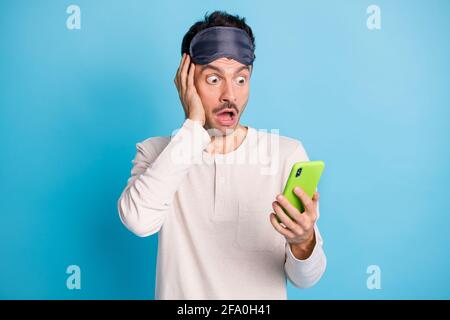 Photo portrait of shocked astonished guy with open mouth touching face holding phone in one hand isolated on vivid blue colored background Stock Photo