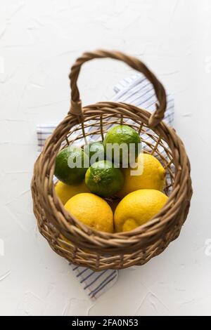 Fresh lemons and limes inside a rustic wicker basket. Stock Photo
