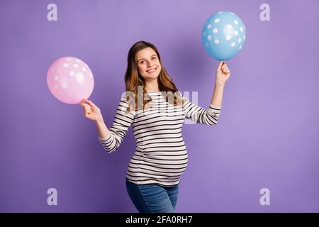 Photo portrait of pregnant woman holding blue and pink balloons isolated on vivid violet colored background Stock Photo