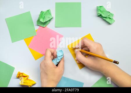 Note paper with a female hand with a pencil and crumpled paper around. The concept of unsuccessful, lost ideas Stock Photo