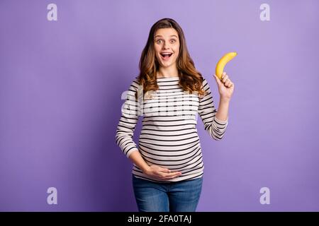 Photo portrait of pregnant girl holding banana isolated on vivid violet colored background Stock Photo