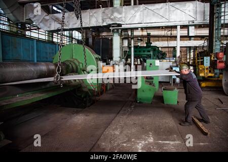 Ust'-Kamenogorsk, Kazakhstan: Vostokmashzavod factory. Heavy engineering plant. Worker in green hardhat bends metal sheet in machine. Stock Photo