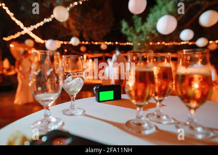 Black digital camera stands on a table covered with a white tablecloth against a background of glasses with drinks Stock Photo