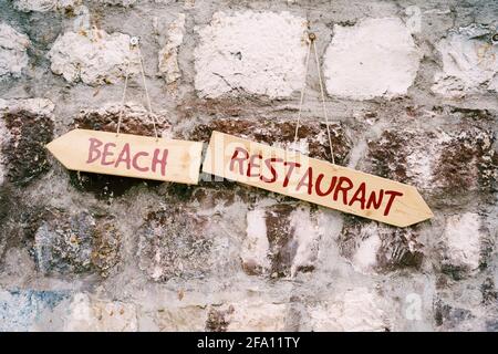 Two multidirectional signs with inscriptions hang on a stone wall. Title: Beach Restaurantt Stock Photo