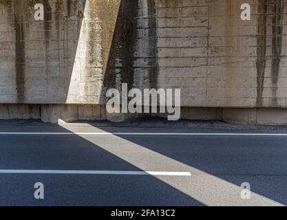 Harsh sunlight falls through the gap between 2 railway tracks  of a bridge, and creates an otherworldly play of light and darkness on the wall and asp Stock Photo