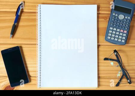 Horizontal top view of rustic wooden business table top with open blank notebook, mobile phone, glasses, pencil and calculator. Home office mockup for Stock Photo