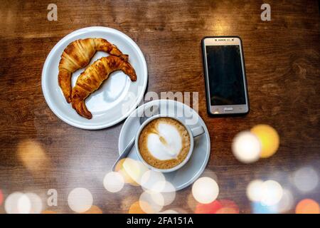 Latte coffee with fat croissants and cell phone.