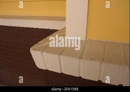 Yellow painted siding joins brown brick at a corner with a prominent white brick ledge. Stock Photo