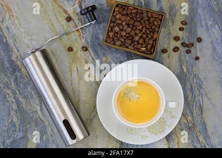 Cup of hot coffee with hand coffee grinder to grind beans. Top view of mini grinding made of steel with handle to make freshly ground coffee drink on Stock Photo