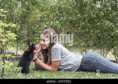 Teenager girl playing with her black rabbit in the garden Stock Photo