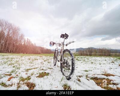 Spring trip with steep mountain bike in snowy landscape.  White mtb with bright  blue hardhat on handlebars. Wild beautiful meadow.