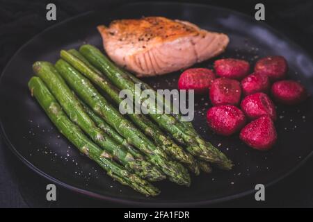 Roasted green asparagus and salmon with beetroot gnocchi on black background Stock Photo