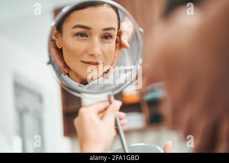 Concentrated lady viewing her reflection in the presence of her cosmetician Stock Photo