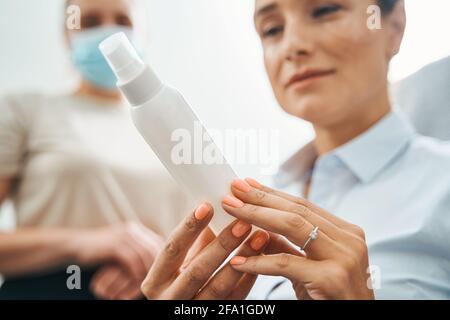 Focused female client viewing a cosmetic product in her hands Stock Photo