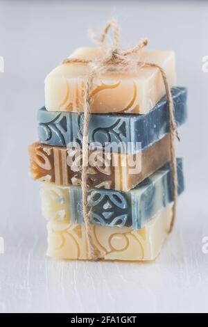 Stack of assorted natural soap bars on white wood. Vertical close-up. Stock Photo