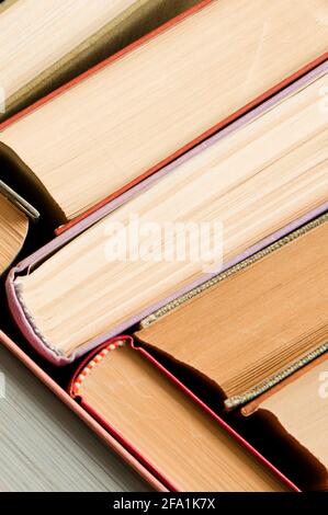 A stack of colorful books in a library or a room. Many multi-colored thick books stands on a dark background. Vertical image Stock Photo