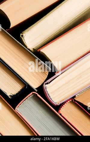 A stack of colorful books in a library or a room. Many multi-colored thick books stands on a dark background. Vertical image Stock Photo