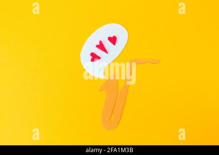 A cutted out of felt saxophone from which hearts flew out, on a yellow background. Flat lay. Jazz Day. Stock Photo