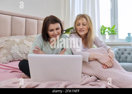 Two middle-aged women withparrot looking at laptop screen sitting in bed at home Stock Photo