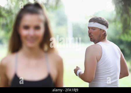 Fat man in sportswear looking at young girl jogging in park Stock Photo