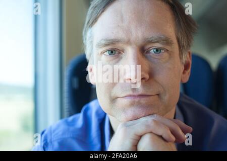 Caucasian man on train leaning forward chin on hand with thoughtful smile looking at camera Stock Photo