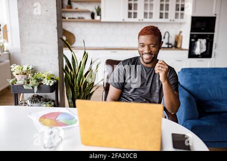 Happy male freelancer using laptop, having a video meeting with coworkers, smiling. Successful businessman discussing a project with colleagues at Stock Photo