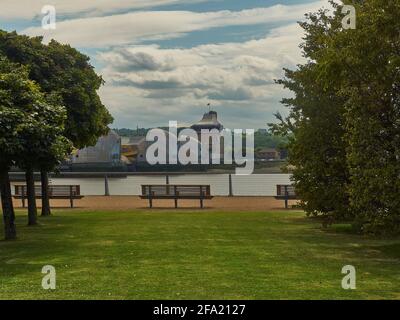 The metallic, alien form of the Thames Barrier, from an avenue of trees on the north side of the river, with summery sky of blue and fluffy clouds. Stock Photo