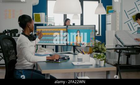 Black retoucher woman analysing images on pc with two monitors and retouching digital assets with stylus pencil. African project designer using photo editing software sitting in creative agency office Stock Photo