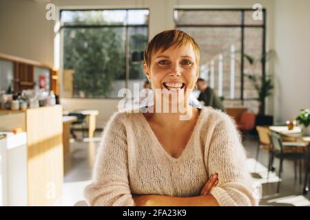 Happy female entrepreneur with arms crossed standing in co-working space. Confident female standing in office. Stock Photo