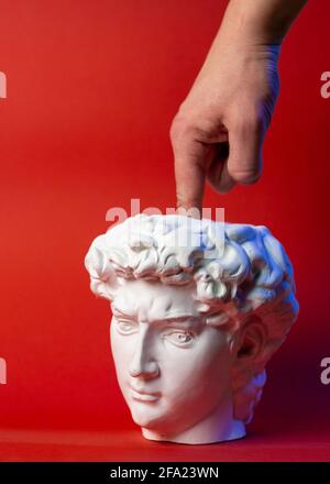 Plaster pot in the form of David's head and male hand on a red background. Stock Photo