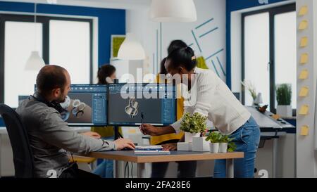Diverse team of engineers working on computer at mechanical piece design cad sharing ideas about industrial project using dual displays setup. Black manager analysing 3D gears on CAD software. Stock Photo