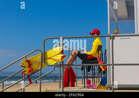 Bournemouth, Dorset UK. 22nd April 2021. UK weather: lovely warm and sunny in sheltered spots, but with a cool breeze; plenty of sunshine and blue skies at Bournemouth beaches, as few visitors head to the seaside to enjoy the sunshine. RNLI Lifeguard keeps a look out at Lifeguards kiosk hut. Credit: Carolyn Jenkins/Alamy Live News Stock Photo