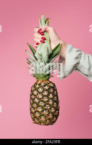 Partial view of woman holding tropical pineapple isolated on pink Stock Photo