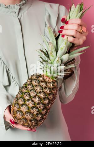 Cropped view of young woman holding exotic pineapple on pink background Stock Photo
