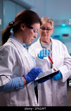 Team of scientist discussing blood analyzis using tablet pc, development. Specialist team of medical researchers working in sterile lab wearing protection glasses. Stock Photo