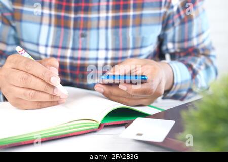 young man hand using smart phone and writing on notepad  Stock Photo