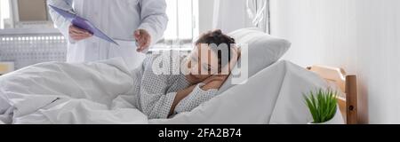 sad african american woman lying in hospital bed near doctor, banner Stock Photo