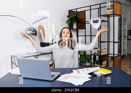 Irritated business woman has messy on the desk, a female employee looking through workpapers on the table, trying to find needed but unsuccessfully, crazy woman throws paper up Stock Photo