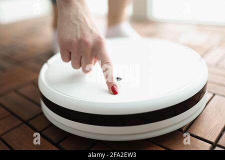 Female finger presses power button on white robotic vacuum cleaner Stock Photo