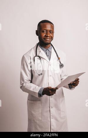 black young smiling doctor stands on a white background with papers in hands Stock Photo