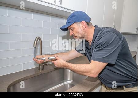 Plumber working on a spray faucet for a kitchen sink in modern home Stock Photo