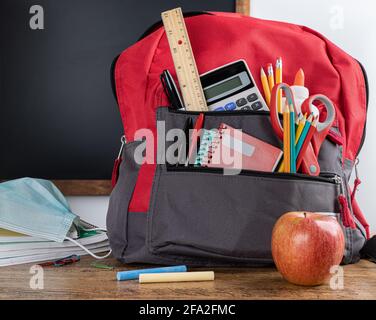 Book bag with school supplies on a desk with blank chalkboard in background Stock Photo