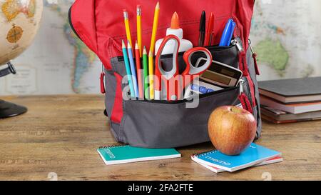 Book bag with school supplies on a wooden table with world map in background Stock Photo