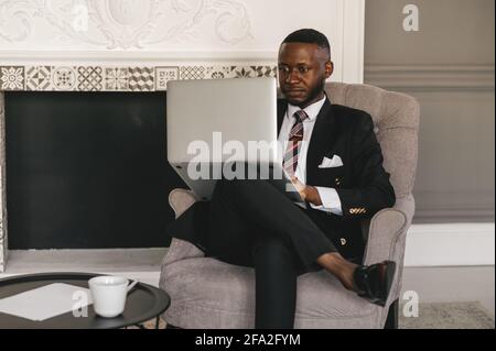 black guy in a black suit sitting in a chair with a laptop Stock Photo