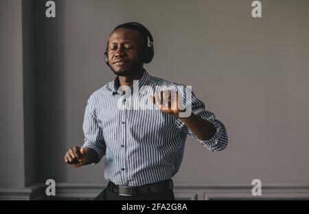 black young man in headphones dancing to the music on a gray background Stock Photo