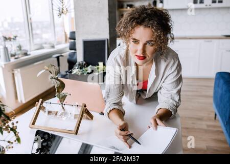 Stylish female freelancer asking an advice from colleague, working on startup, making notes about ideas. Attractive young business woman sitting at Stock Photo
