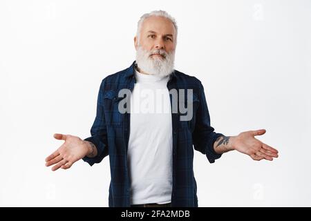 Dont know. Clueless senior man with tattoos, shrugging shoulders and looking confused, being puzzled or unaware, have no idea, dont understand Stock Photo