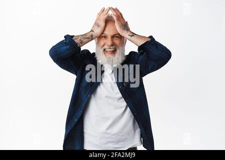 He cant believe it. Excited and surprised old man winning something, holding hands on head and smiling amazed, look with disbelief and happiness Stock Photo
