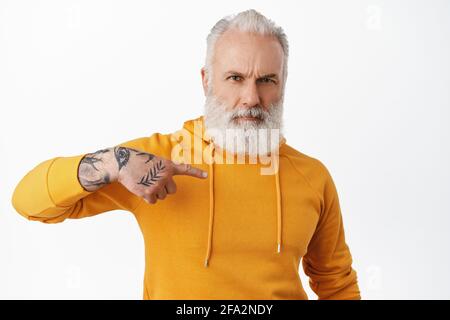 Serious and confident hipster senior man point at himself. Old guy with tattoos pointing at him and frowning, looking determined, you need me gesture Stock Photo